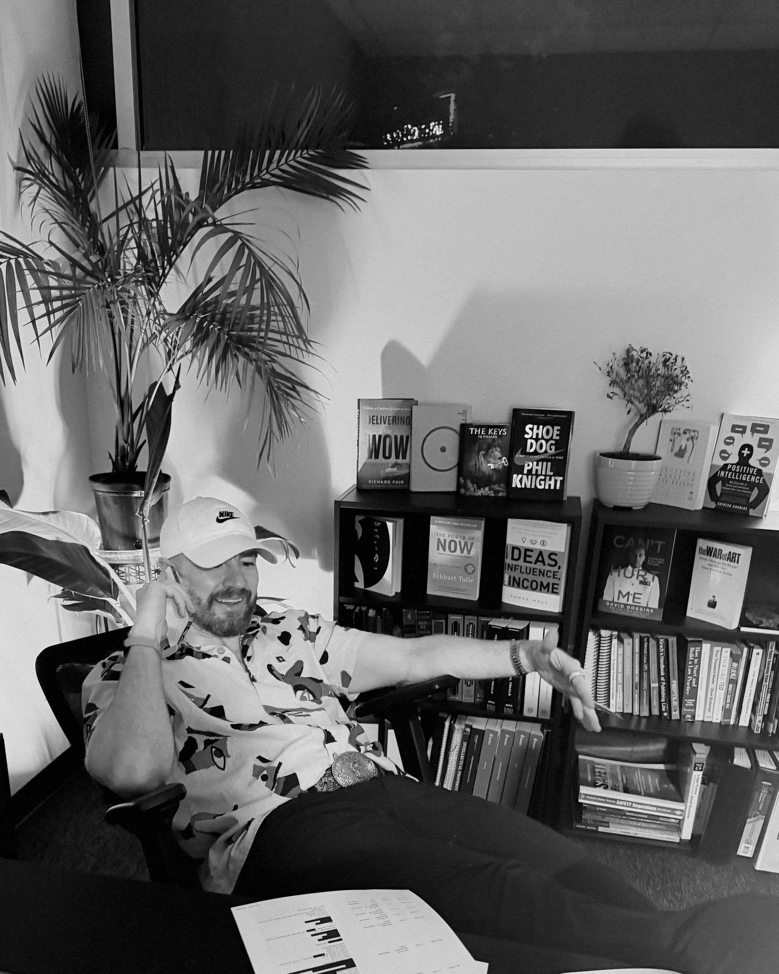 Guy Muller in a ball cap in his home studio, a bookshelf with Shoe Dog visible behind him