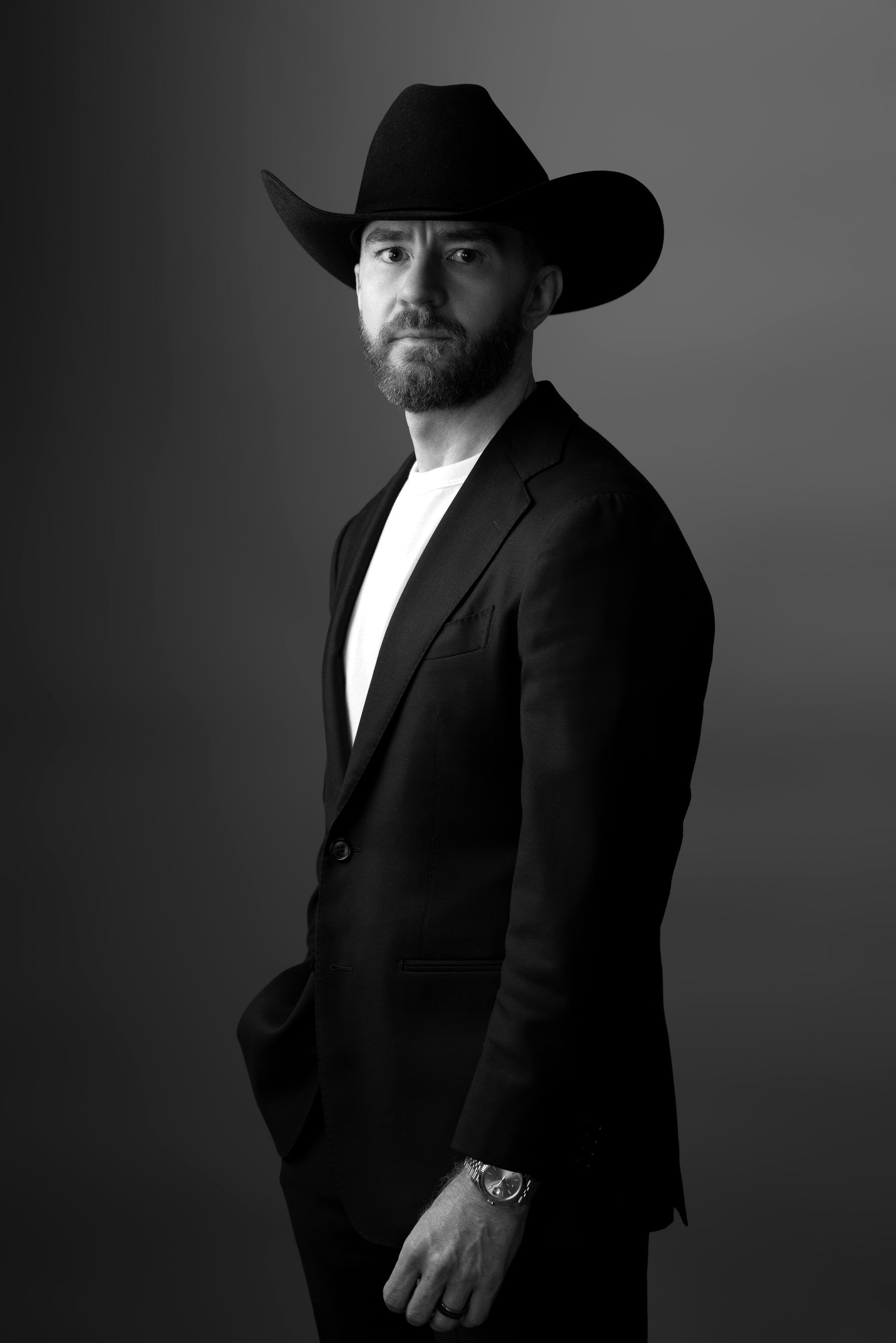 Guy Muller in a black cowboy hat and white tee, standing in dramatic side light